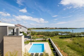 A modern house with a swimming pool, a view of the sea, and a garden.