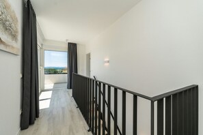 A modern interior with a wooden floor, a black railing, and a view through a glass door to the outside.