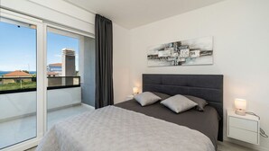 Een moderne slaapkamer met een groot bed, een nachtkastje, een wandlamp en uitzicht op gebouwen door een glazen schuifdeur.