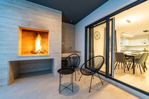 A modern living area with a fireplace, two black chairs, and a dining area visible through glass doors.