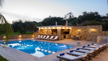Piscina com espreguiçadeiras e área de cozinha ao ar livre com construção em pedra.