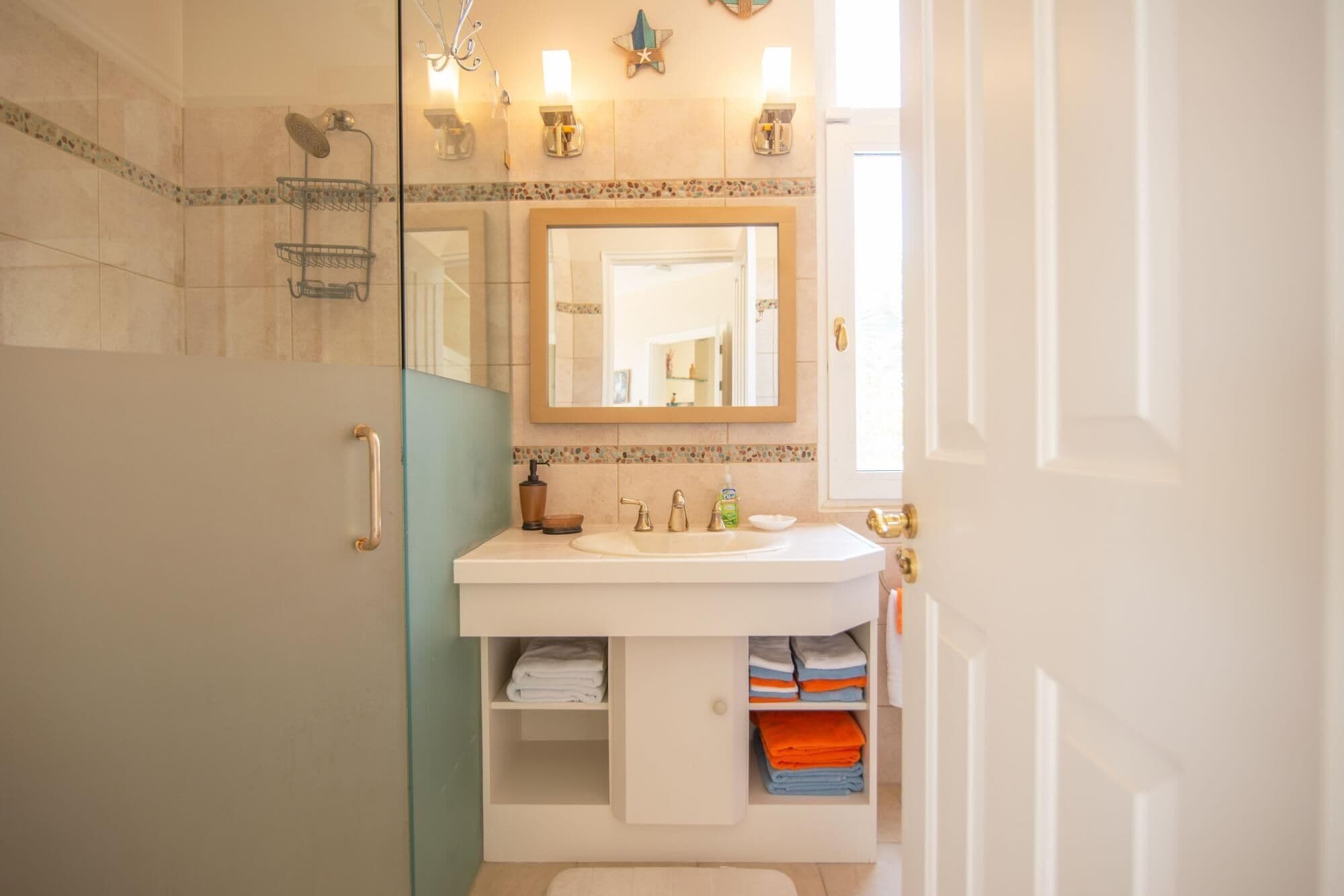 A bathroom with a glass shower enclosure, a white sink with a mirror above it, and a towel rack.