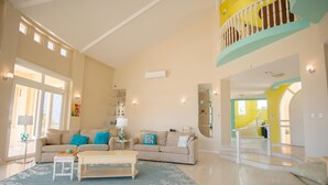 A spacious living room with a high ceiling, a staircase leading to an upper level, and a large window providing natural light. - This One of a Kind Amazing Aruba Beach House (Noord)
