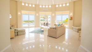 A spacious living area with a large window overlooking a pool and beach, a ceiling with skylights, and a sign reading "Beach House". - This One of a Kind Amazing Aruba Beach House (Noord)