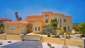 A large, yellow building with a red-tiled roof, multiple windows, and a gated entrance. - This One of a Kind Amazing Aruba Beach House (Noord)