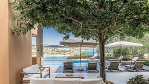 A poolside area with lounge chairs, umbrellas, and a view of the sea. - Chloe Seafront Villa (Chania)