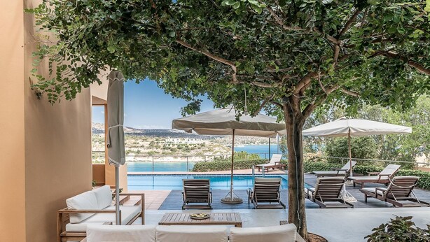 A poolside area with lounge chairs, umbrellas, and a view of the sea. - Chloe Seafront Villa (Chania)