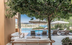 A poolside area with lounge chairs, umbrellas, and a view of the sea. - Chloe Seafront Villa (Chania)