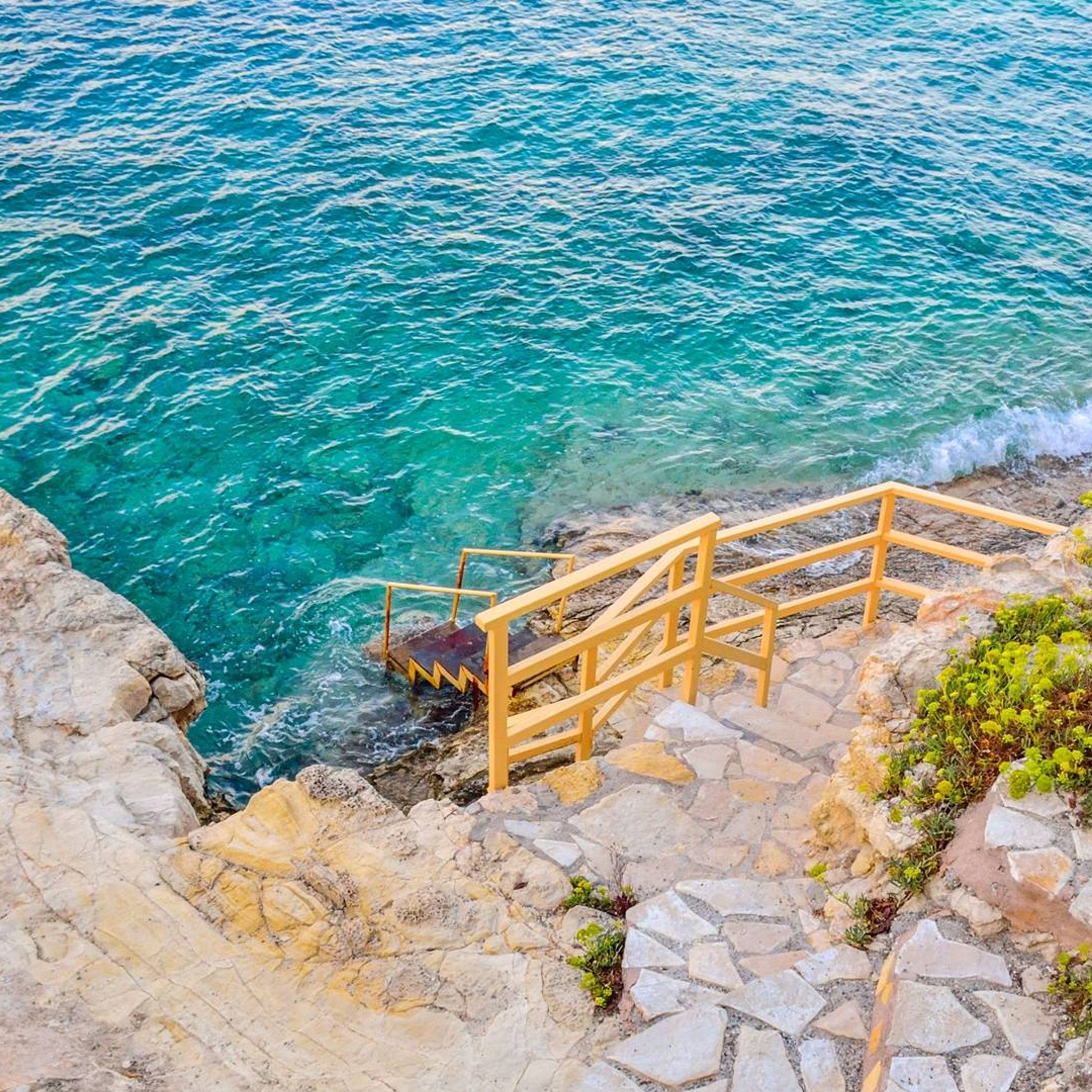 A stone staircase leading to a rocky shore with clear blue water.