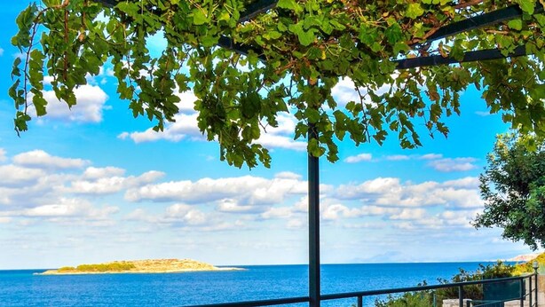 An outdoor dining table with a view of the sea, a bottle of wine, and a bowl of fruit. - Chloe Seafront Villa (Chania)