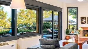 A modern living room with a large window, a sofa, a table, and a fireplace. - Chloe Seafront Villa (Chania)