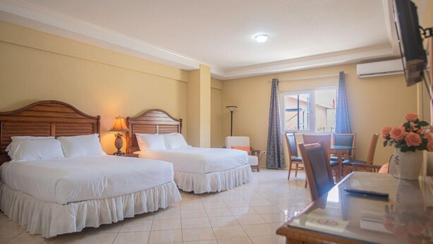 A hotel room with two beds, a desk, a chair, a lamp, and a window with curtains. - NEW Bay Harbor Studio 201 4 Persons (Oranjestad)