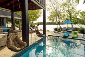 Zona de piscina con sillones de descanso, una hamaca colgante y vistas al agua.