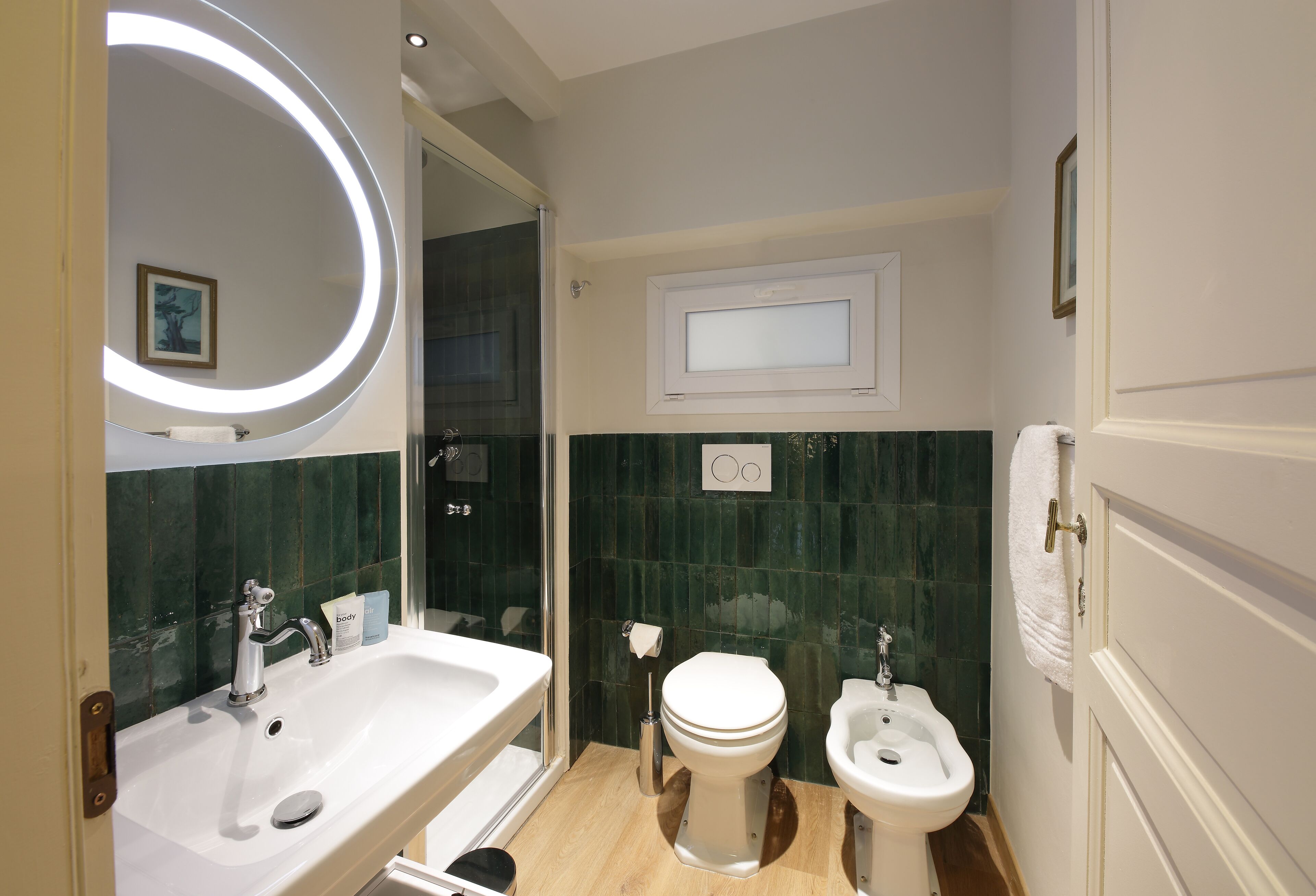A bathroom with a sink, toilet, bidet, and a mirror with a circular light.