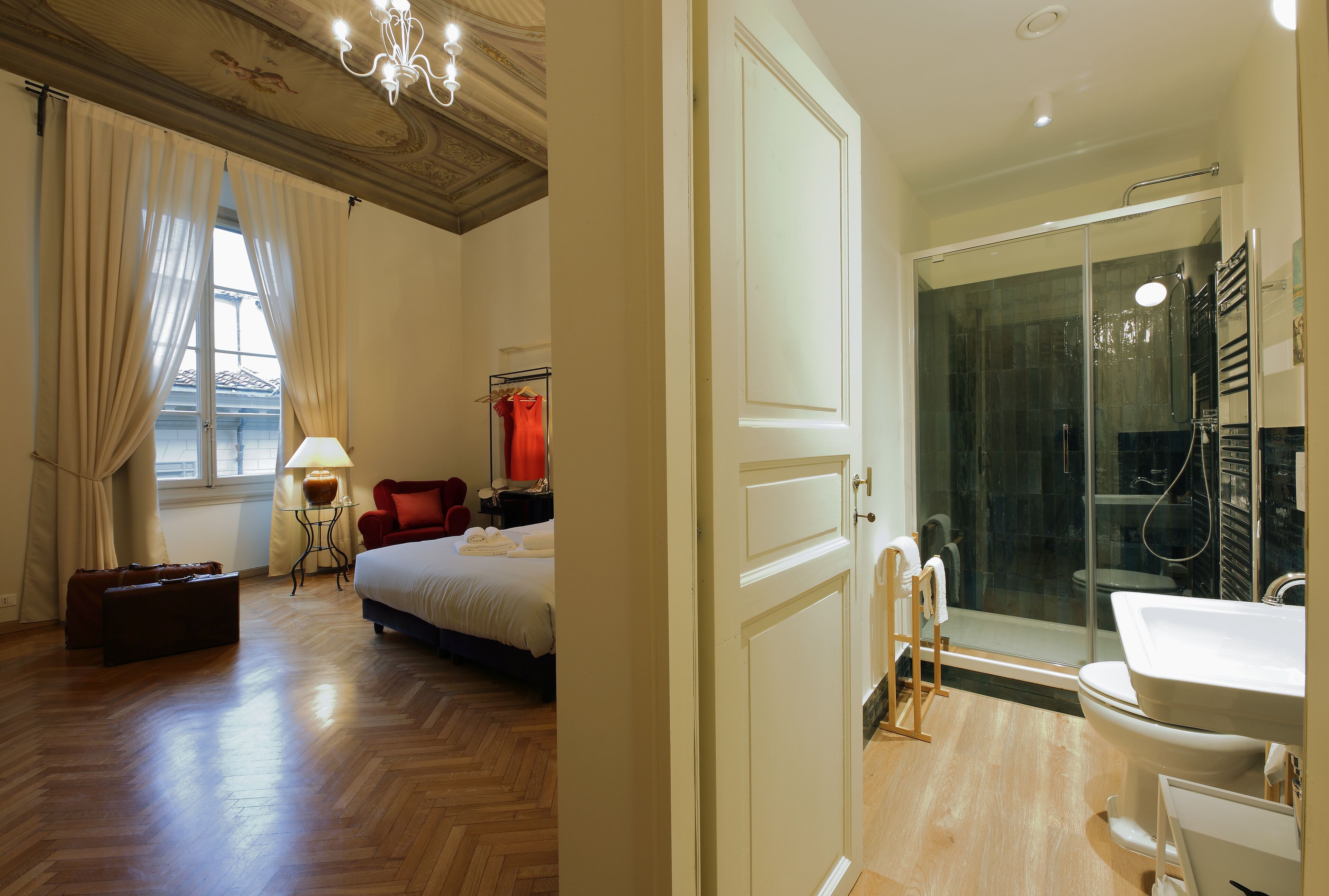Ein Hotelzimmer mit Bett, Koffer, Lampe, Stuhl und einem Badezimmer mit Dusche und Waschbecken.
