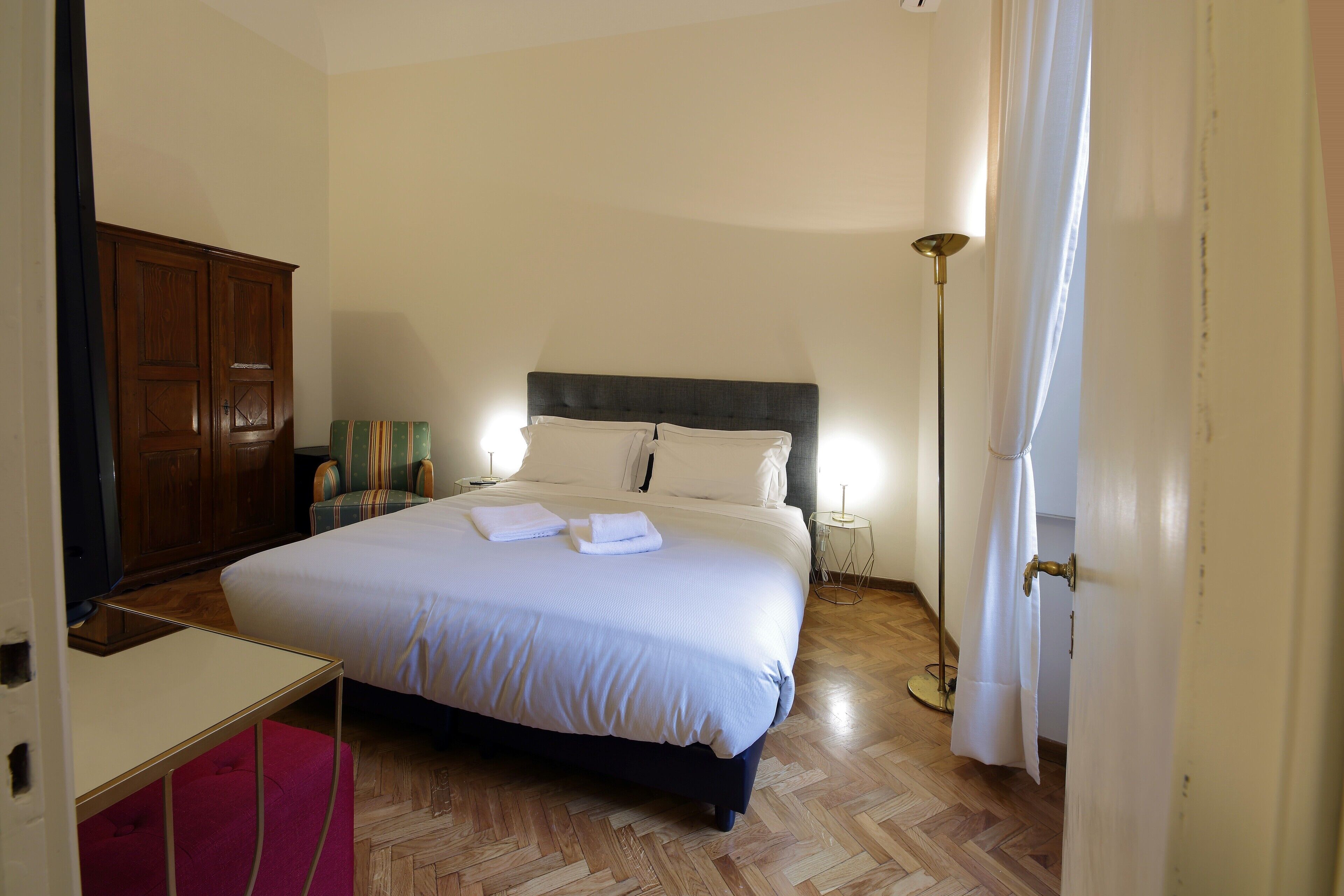 A hotel room with a bed, bedside table, wardrobe, and a floor lamp.