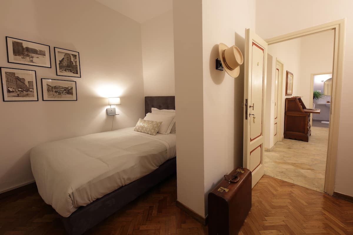 Quarto com cama, mesa de cabeceira, luminária na parede e quadros decorativos.