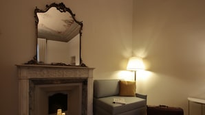 Una habitación con chimenea, un sofá, una lámpara y una maleta.