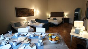 Habitación de hotel con dos camas, una mesa de comedor con desayuno servido y un cuadro en la pared.