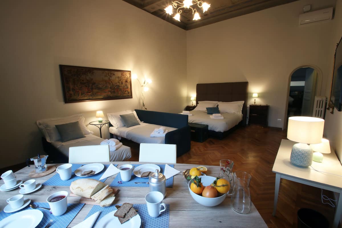 Quarto de hotel com duas camas, uma mesa de jantar posta para o café da manhã e um quadro na parede.