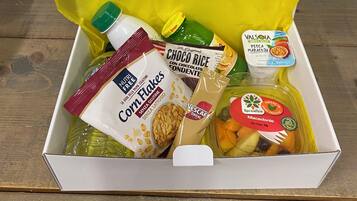 A box of groceries including corn flakes, choco rice, and a bottle of milk.