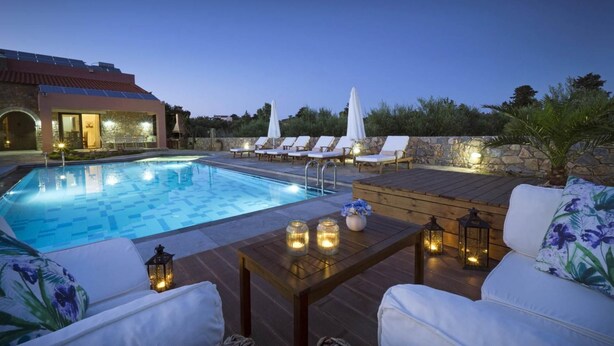 A poolside area with lounge chairs, a wooden deck, and a stone wall. - Nafsika Villa in Litsarda (Apokoronas)