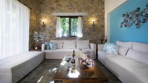 A living room with a stone wall, two sofas, a coffee table with wine glasses, and a blue accent wall. - Nafsika Villa in Litsarda (Apokoronas)