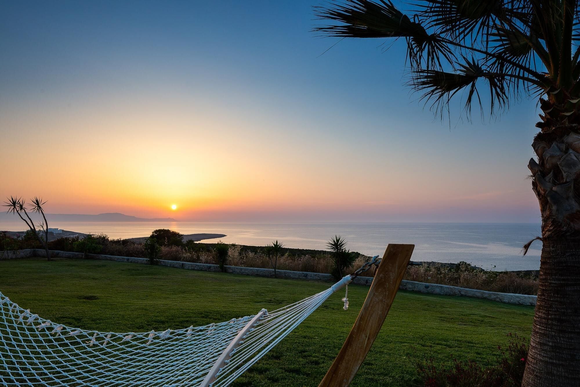 Un hamac installé sur une pelouse, d’où l’on peut admirer le coucher de soleil sur la mer.