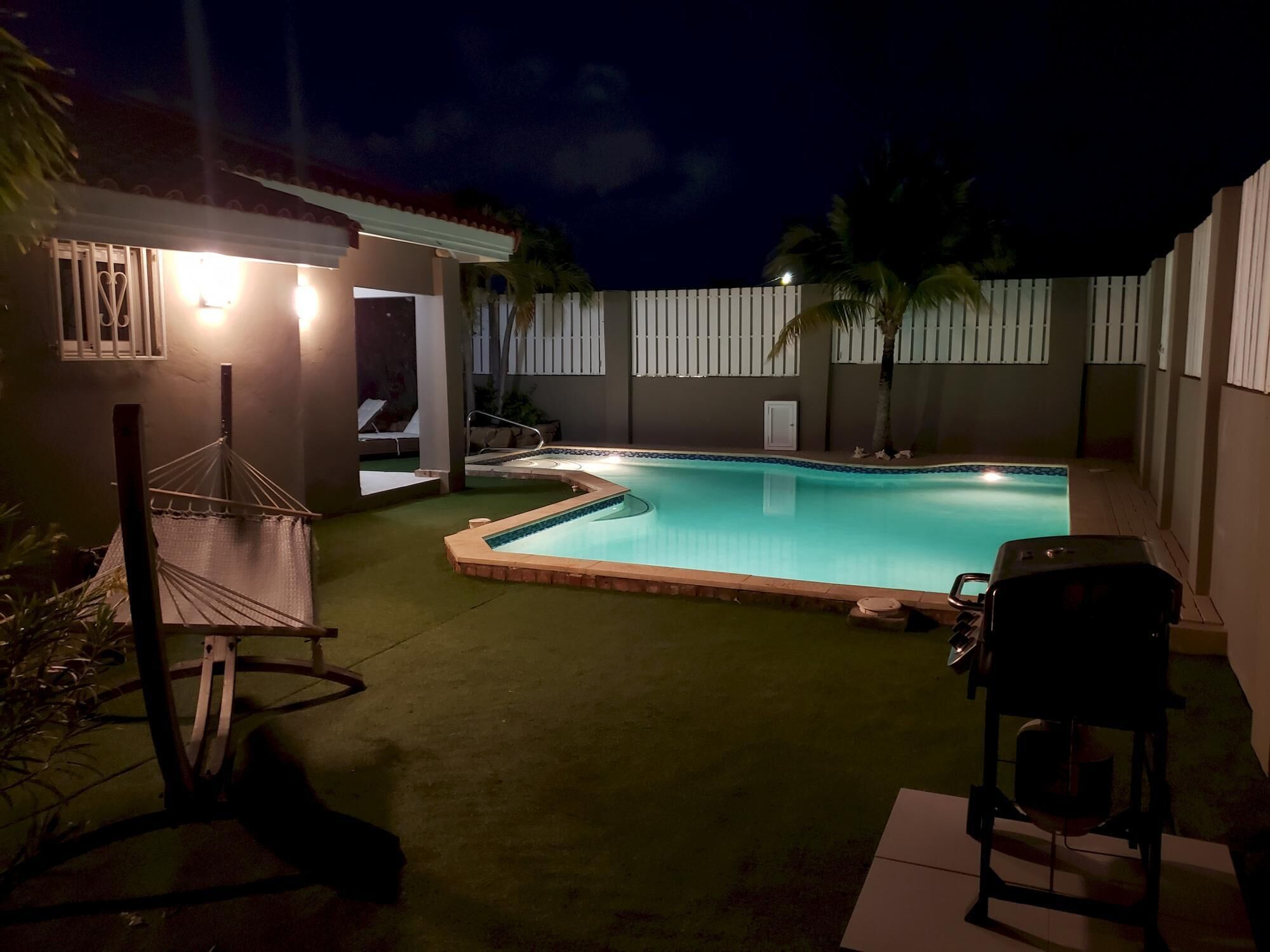 Una piscina con una pequeña terraza, una hamaca y una parrilla.