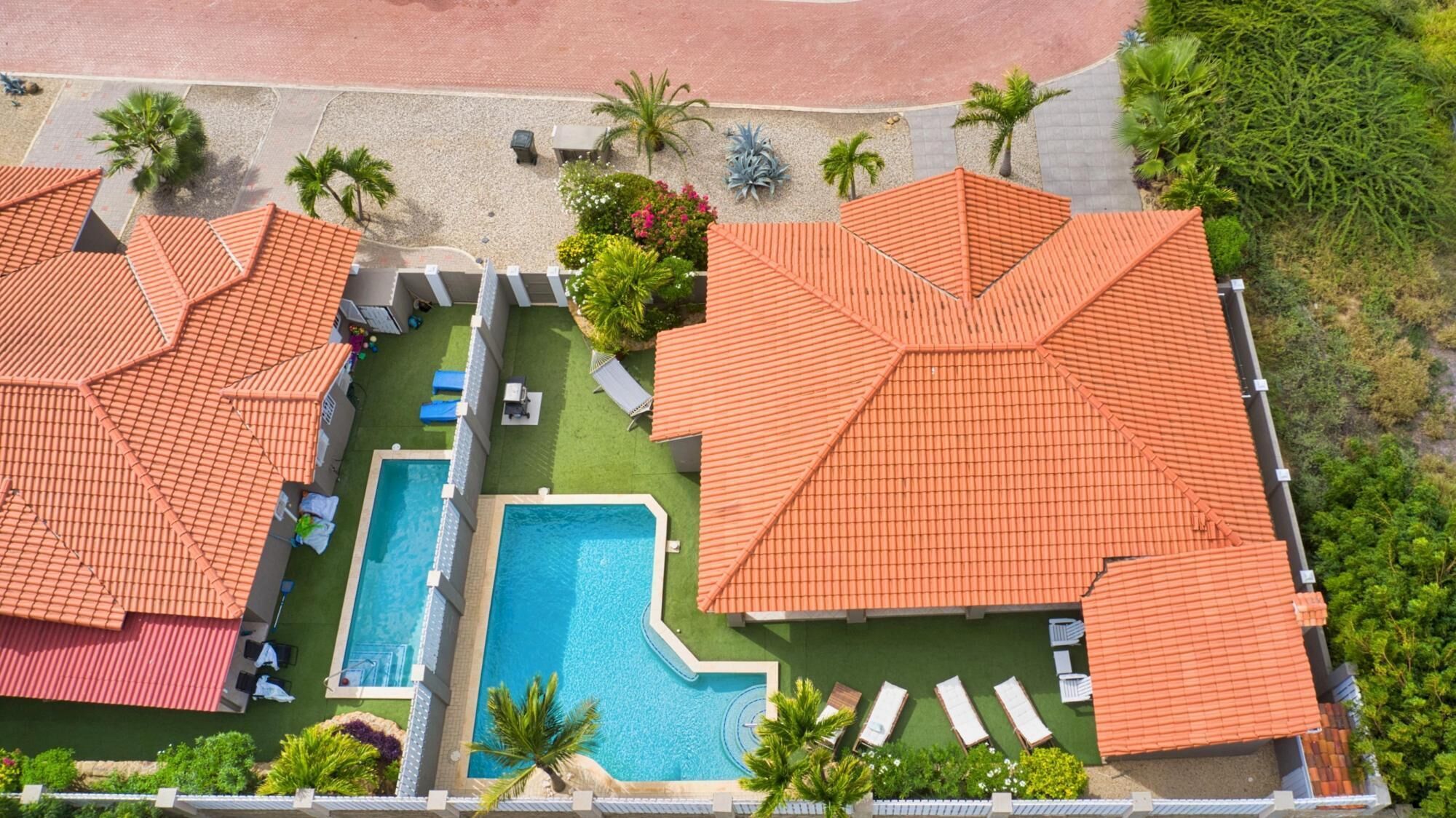 An aerial view of a resort with two swimming pools, multiple lounge areas, and a beach area.