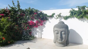 A Buddha statue in a garden with a white wall and flowering plants. - Palm Beach 34 Suitable for 8 Persons 4 Bedrooms 4 Bathrooms (Noord)