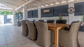 A covered patio area with a wooden table and wicker chairs, a 'HOME' sign, and a clock on the wall. - Palm Beach 34 Suitable for 8 Persons 4 Bedrooms 4 Bathrooms (Noord)