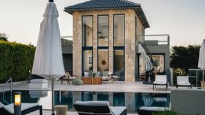 Ein modernes Haus mit Pool, Sitzgelegenheiten im Freien und einer großen Glasdoor.