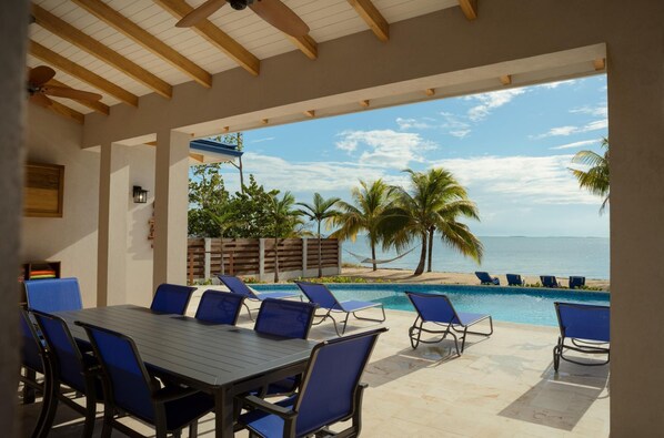 A covered outdoor area with a pool, lounge chairs, and a table with chairs. - South Gull House in Belize City (Placencia)