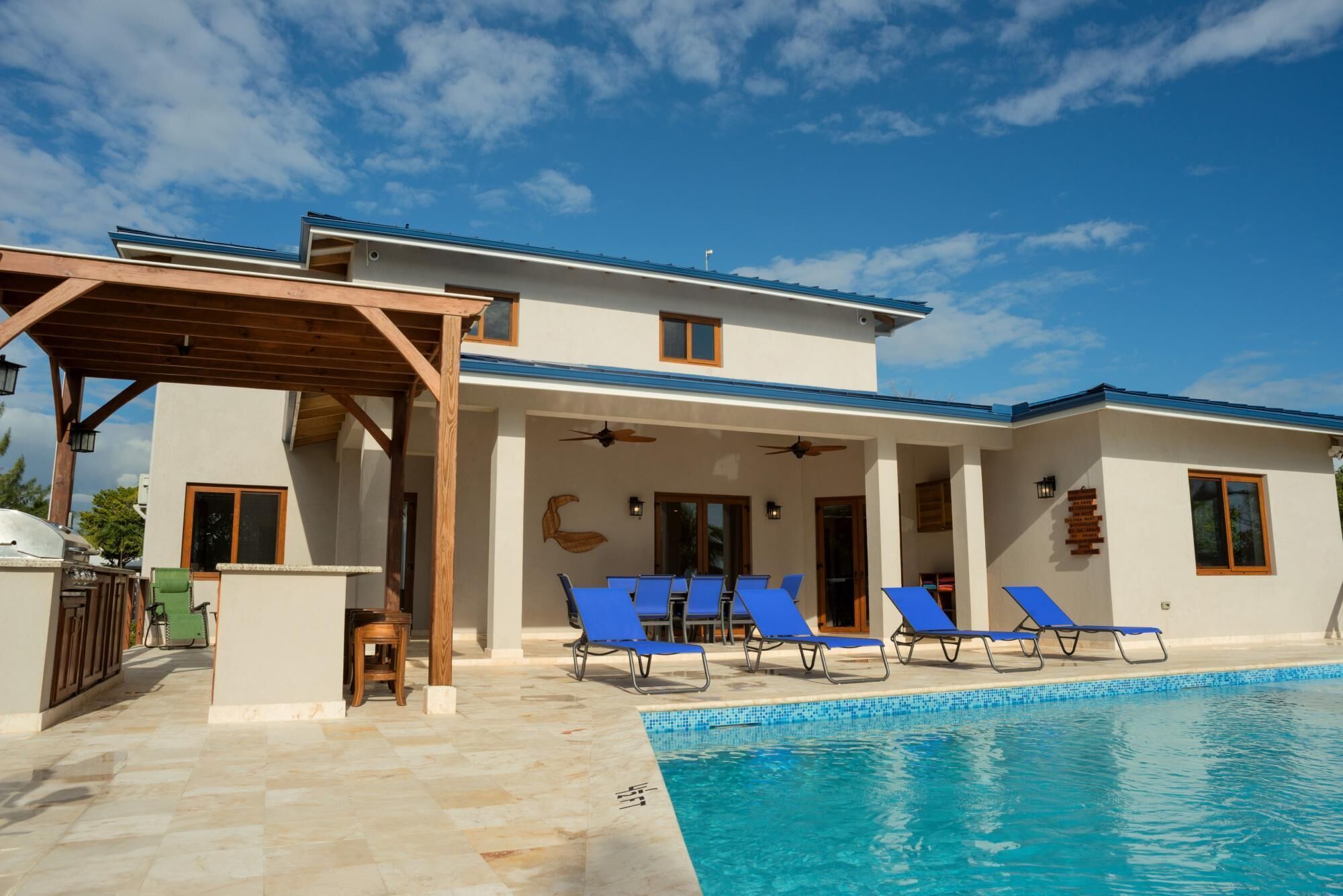 A modern two-story house with a swimming pool, blue lounge chairs, and a pergola.