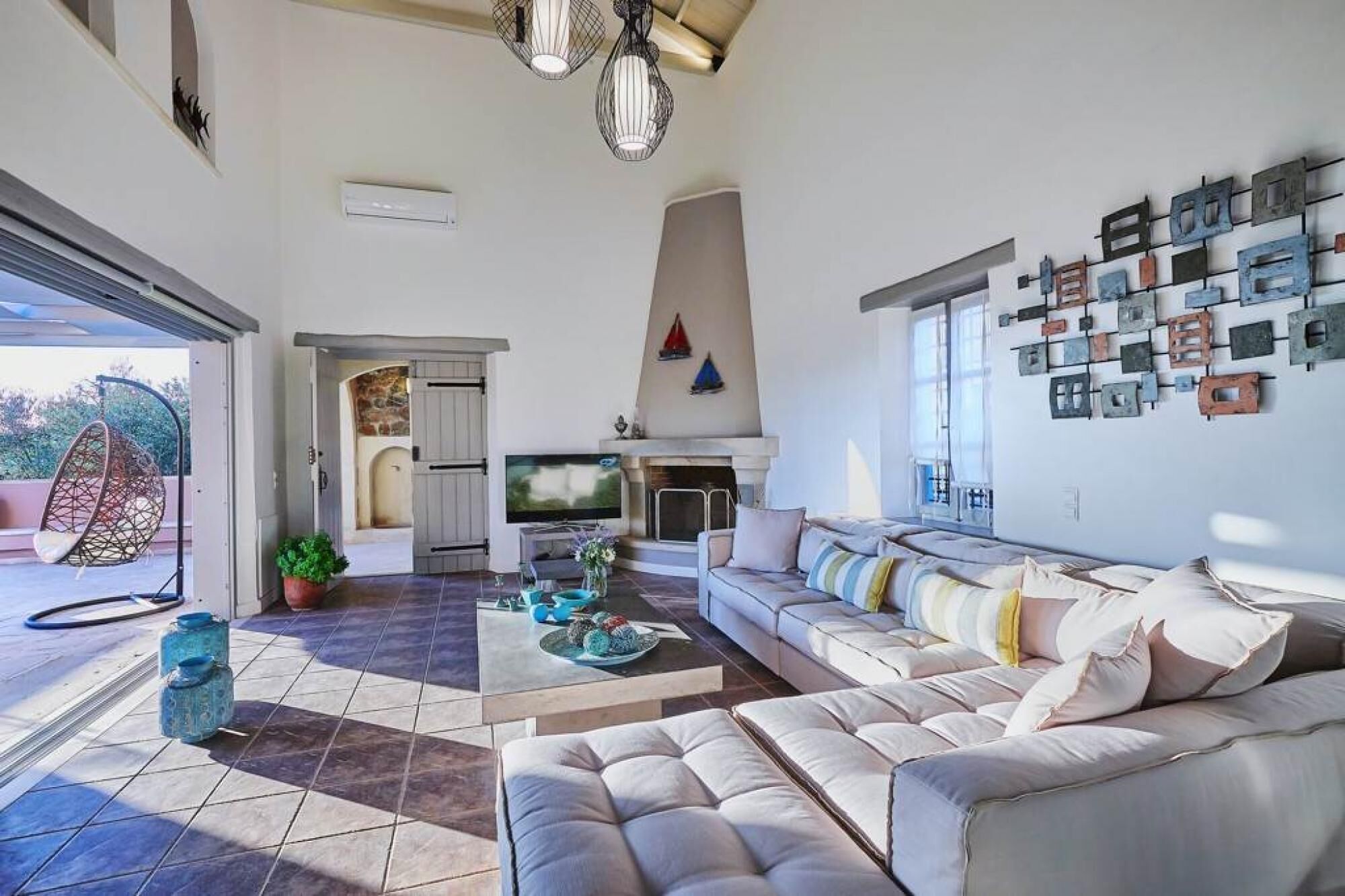 Ein geräumiges Wohnzimmer mit einer großen Couch, einem Kamin und einem Fernseher. Es gibt einen Essbereich mit Tisch und Stühlen sowie einen Balkon mit einer Hängesitzgelegenheit.