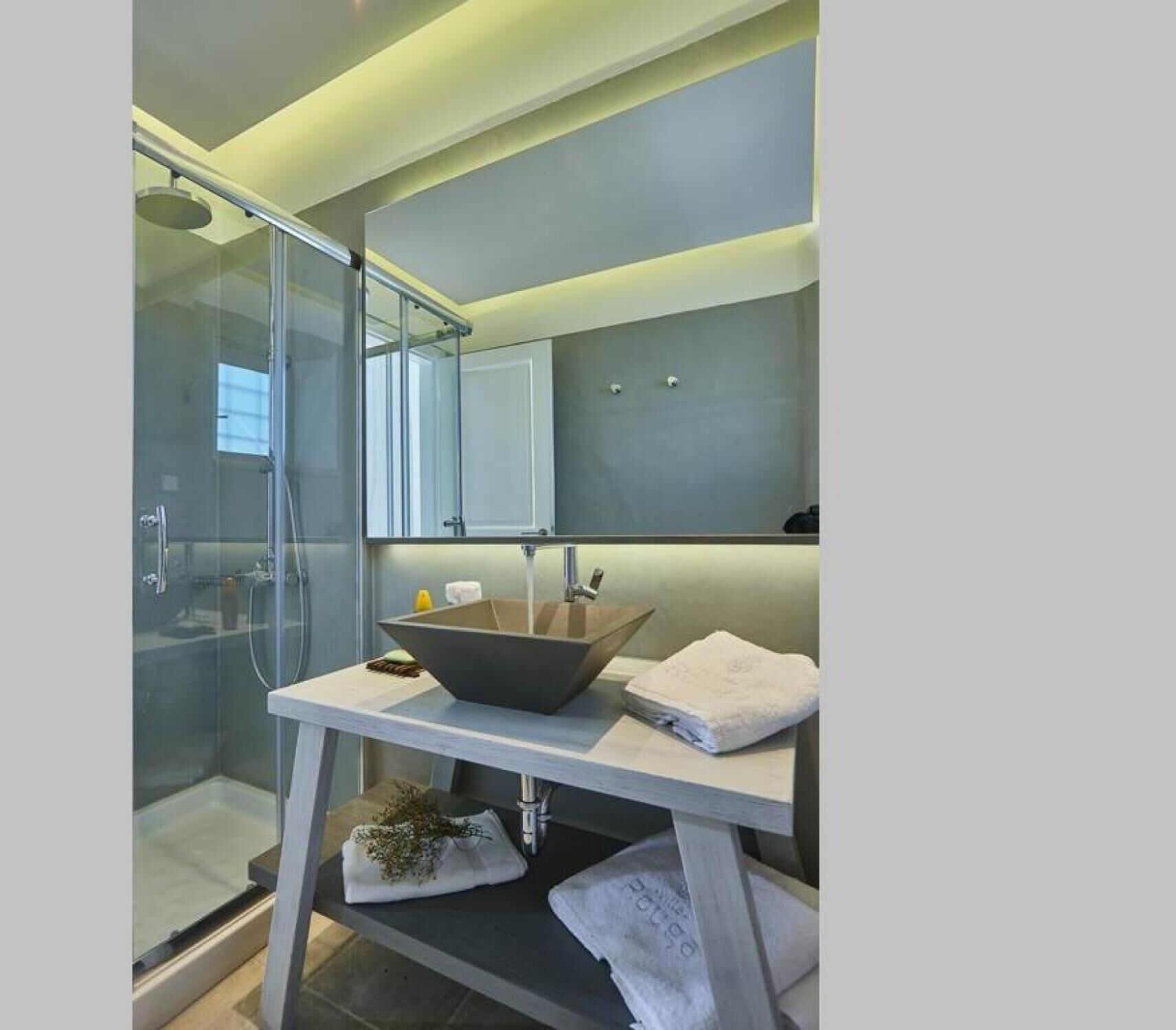 A modern bathroom with a glass shower enclosure, a vessel sink, and a mirror above the sink.