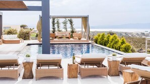 A poolside area with lounge chairs, a pergola, and a view of the sea. - Jamila Villa in Kalathas (Chania)