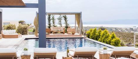 Una zona de piscina amb gandules, una pèrgola i vista al mar.