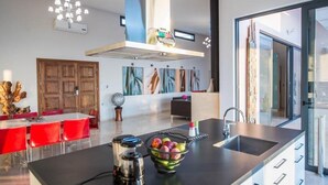 A modern kitchen with a central island, a built-in oven, and a large window providing natural light. - Jamila Villa in Kalathas (Chania)