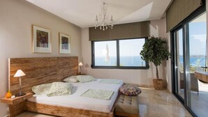 A bedroom with a large bed, a chandelier, a potted plant, and a view of the sea through a large window. - Jamila Villa in Kalathas (Chania)
