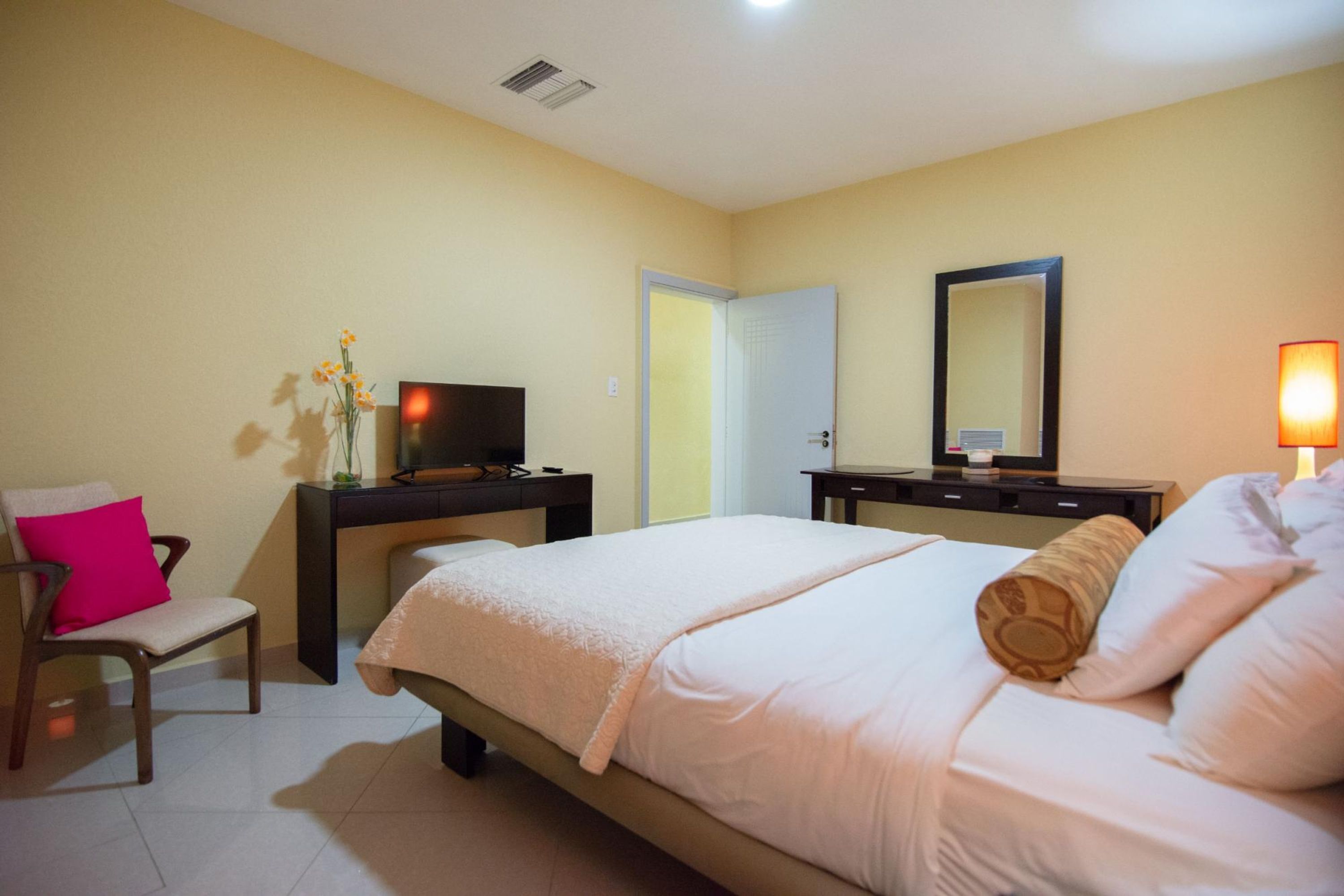 A hotel room with a bed, a desk, a chair, a TV, and a mirror.