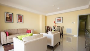 A modern living room with a beige sofa, a white armchair, and a dining area with a table and chairs.
