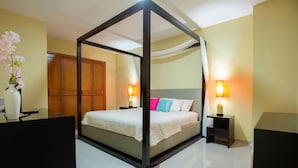 A bedroom with a four-poster bed, bedside tables with lamps, a wooden wardrobe, and a vase with flowers on a nightstand.