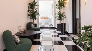 A hallway with a black and white checkered floor, green armchairs, a chandelier, and wall-mounted sconces. - Holt Hotel De Mi Independencia (Oaxaca)
