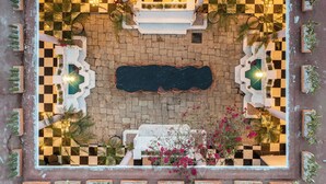 An outdoor patio area with a checkered floor, surrounded by planters with various plants, a central seating area with tables and chairs, and a pool. - Holt Hotel De Mi Independencia (Oaxaca)