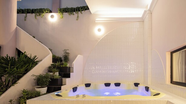 A modern outdoor hot tub area with a spiral staircase, surrounded by potted plants and a tiled wall. - Holt Hotel De Mi Independencia (Oaxaca)