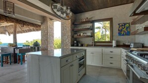 A modern kitchen with a stone column, built-in appliances, and a view of the ocean. - Gladden Caye Private Island Resort (Placencia)
