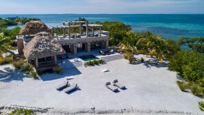 A beachfront property with a pool, lounge chairs, and a thatched-roof structure. - Gladden Caye Private Island Resort (Placencia)