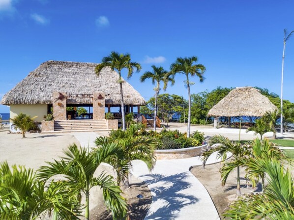 A resort with thatched-roof buildings, palm trees, and a clear blue sky.